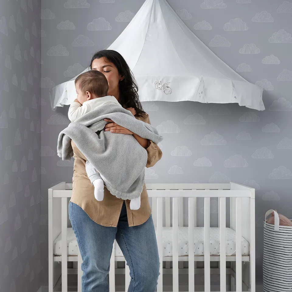 Mother holds baby near crib with soft, sustainable blanket.