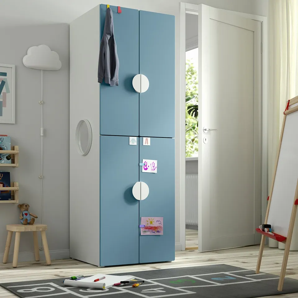 Childs room with blue SMÅSTAD wardrobe, large, near door, hanging coat, with drawers, stickers, art supplies.