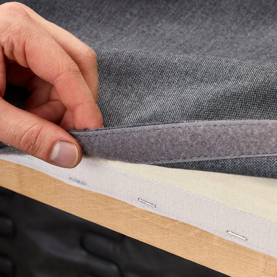 Hand lifting grey fabric panel, revealing underside of sofa cover, showcasing durable, machine-washable material.