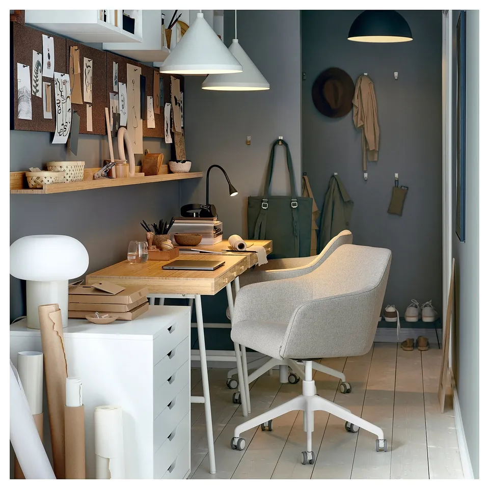 Home office with TOSSBERG swivel chair in grey fabric, white desk, wooden shelves, hanging coats, and pendant lights.