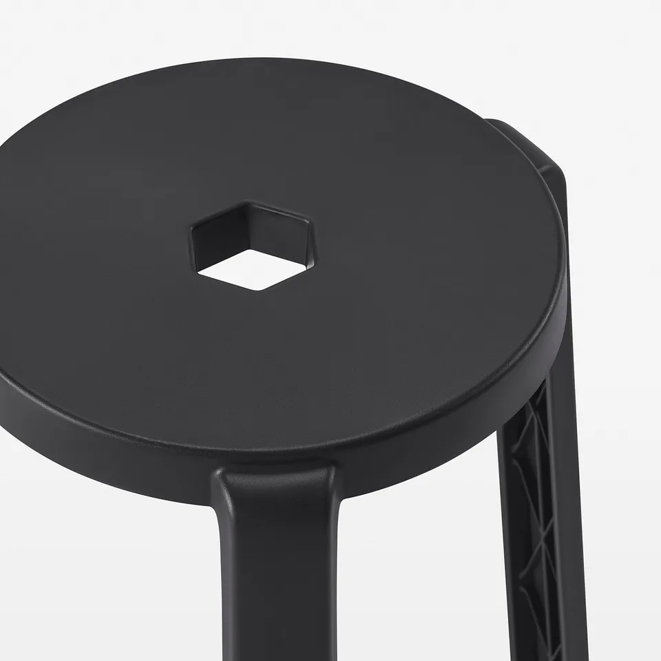 Black stool with circular seat and three legs. Central cutout for stability. Modern design, sturdy construction.