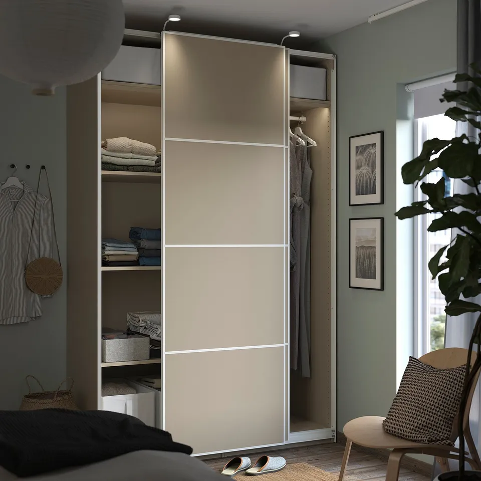 Modern bedroom with PAX wardrobe, open door showing clothes, striped shirt, and plant.