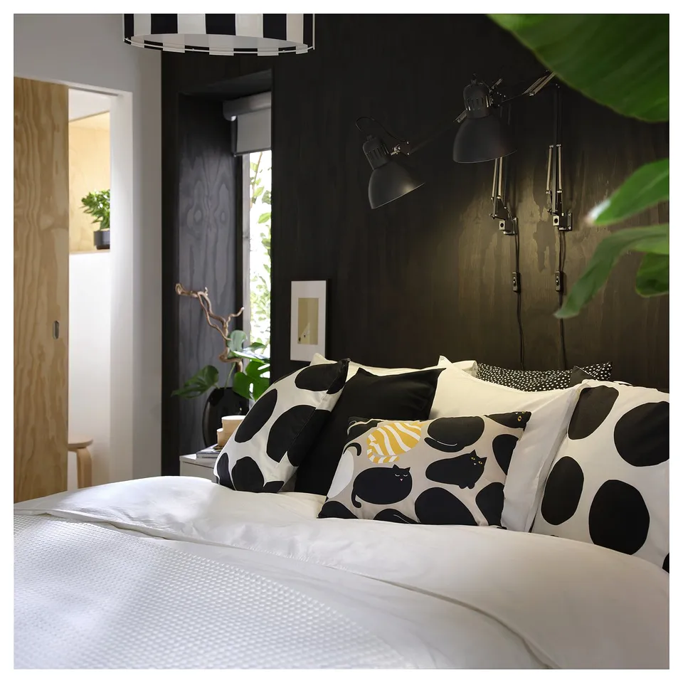 Cosy bedroom with cat-themed pillows on bed, hanging lamps, and plants.