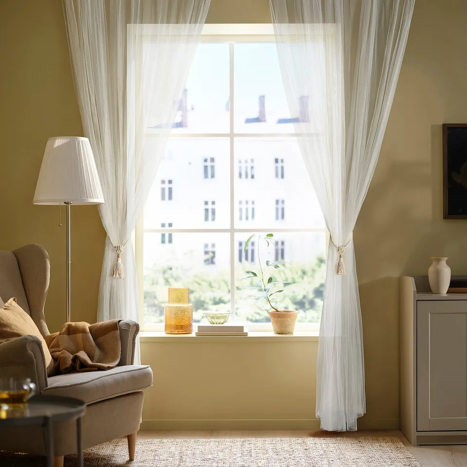 Living room with DUNFLÄTA curtains, armchair, blanket, and lamp.