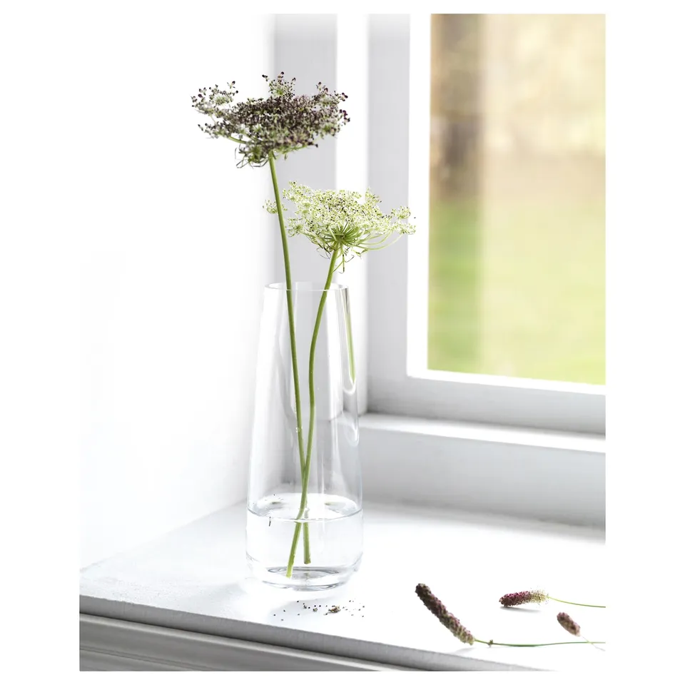 Vase with flowers on windowsill, purple and green stems.