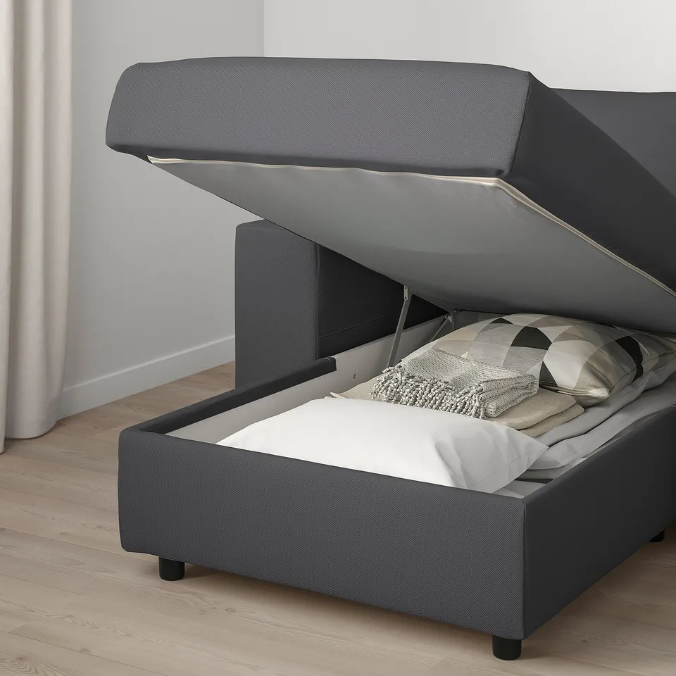 Modern grey sofa with raised seat revealing storage space with blankets inside.