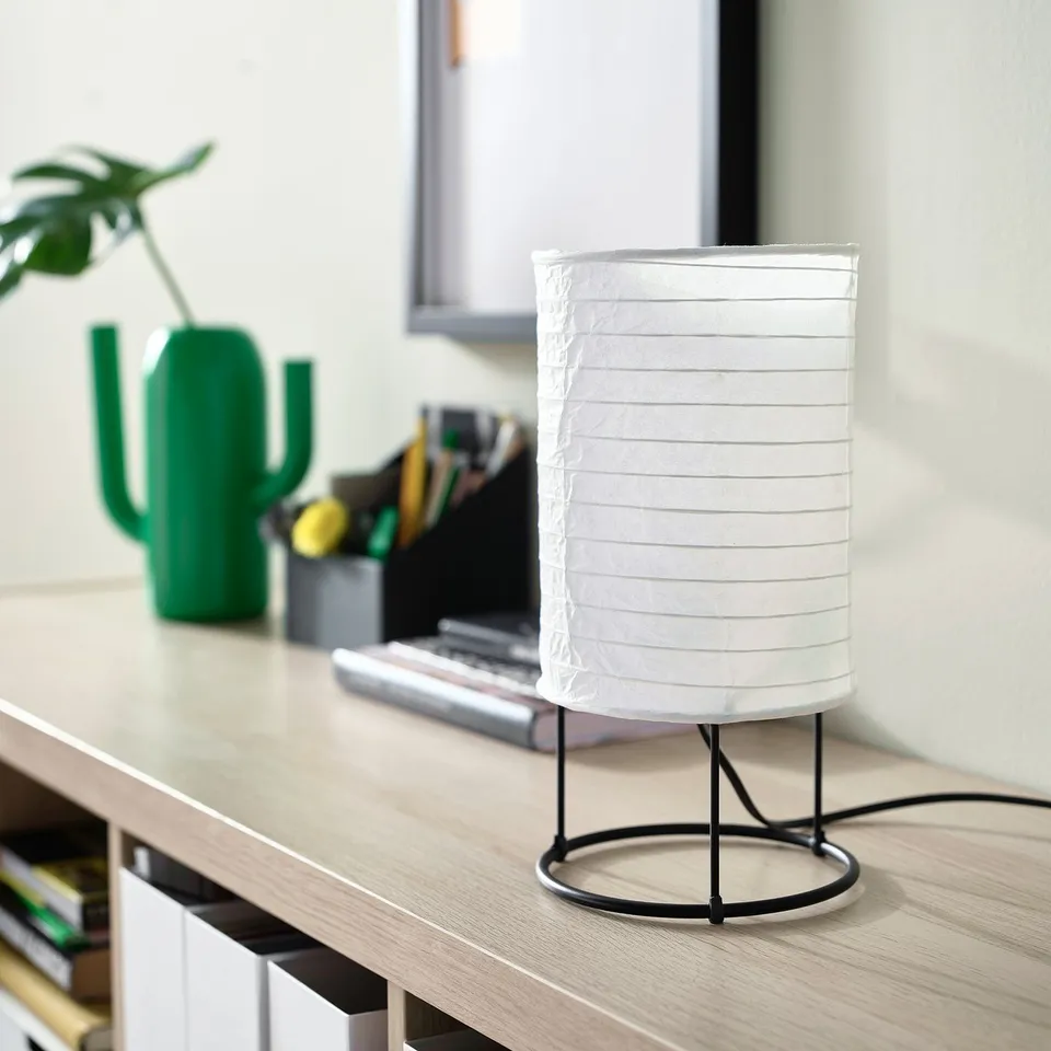 STRANDAD white lamp on desk, small, rice paper shade, black metal base. Next to green cactus and laptop.