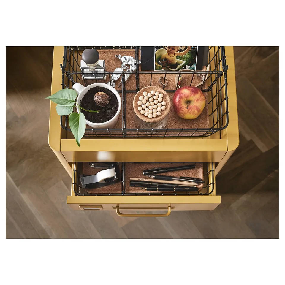 The IDÅSEN unit in yellow holds items. An open drawer reveals pens and a closed one has a basket with snacks and an apple.