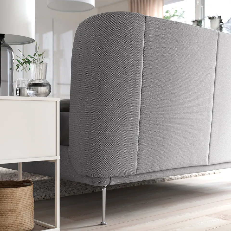 Grey bed with curved headboard and metal legs, white bedside table with vase.