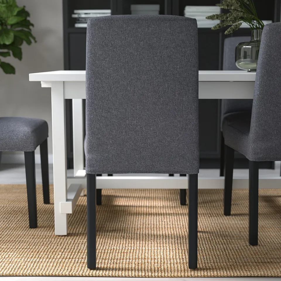 Modern dining set with 3 grey chairs & black legs around white table on rug.
