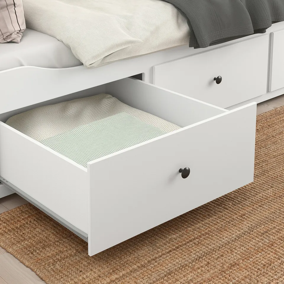White bed drawers open, filled with folded blankets. Black knobs on drawer fronts.