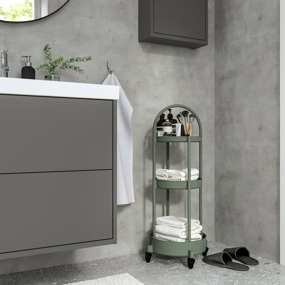Modern grey-green 3-tier JUTTERSBO trolley next to bathroom vanity, holding towels and toiletries.