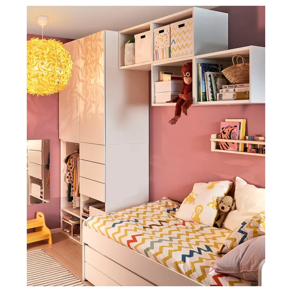 Childs bedroom with pink walls, vibrant bedding, and a hanging monkey toy. White storage units with colourful boxes and a yellow lamp.