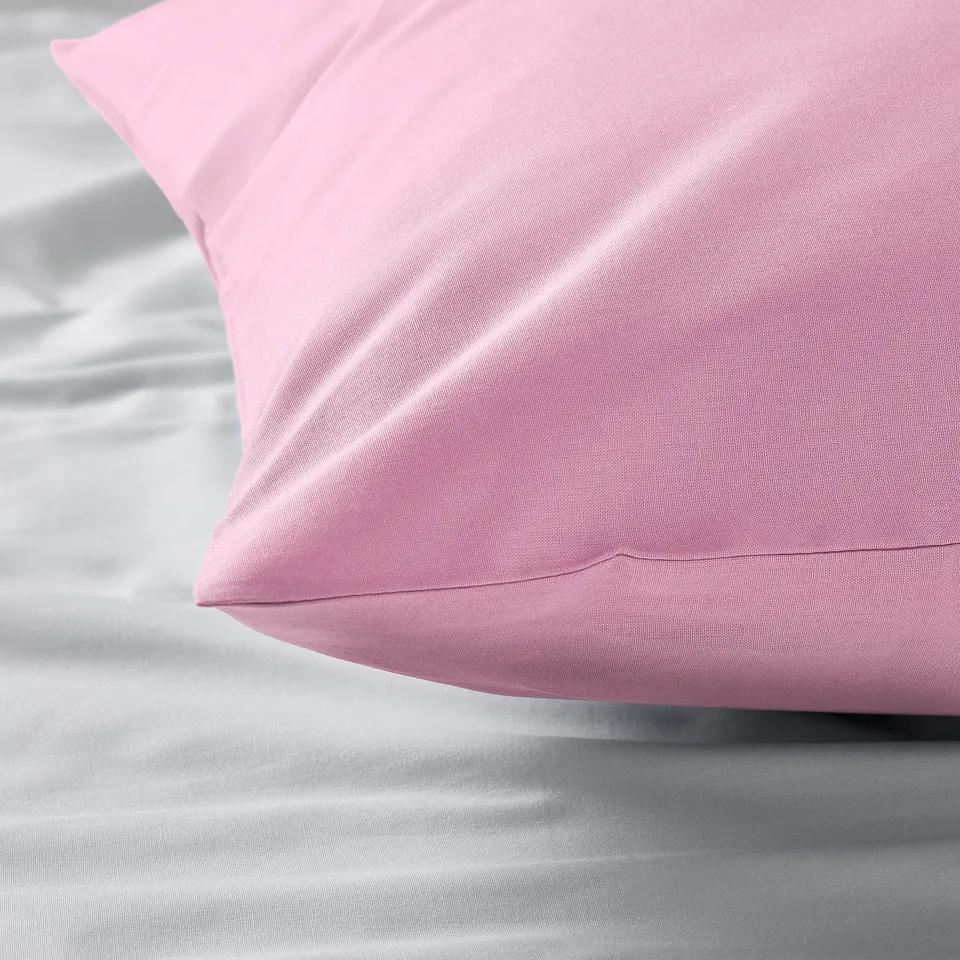 Close-up of smooth, pink cotton pillowcase on bed.