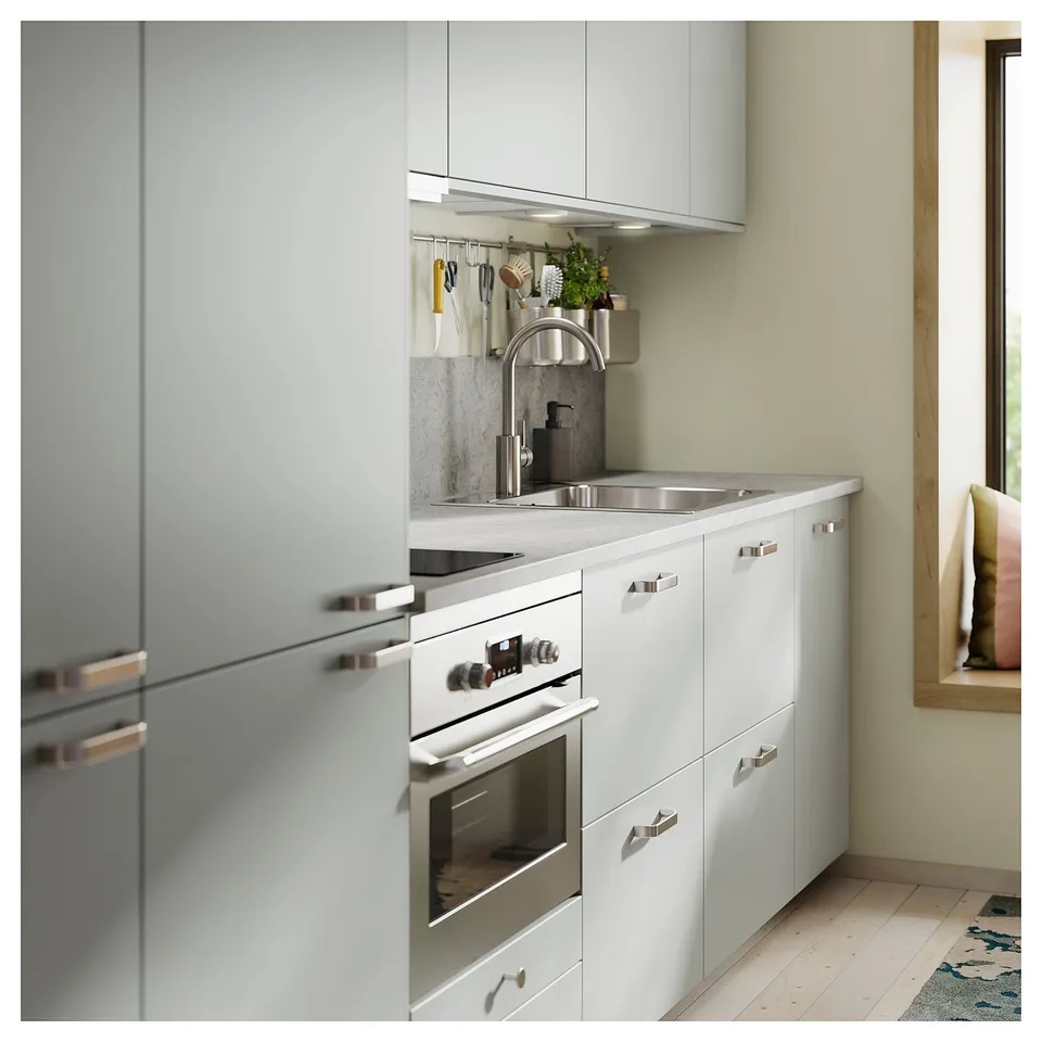 Modern kitchen with light grey cabinets, stainless steel appliances, and sleek metallic handles. A clean and minimalist design with wooden floors.