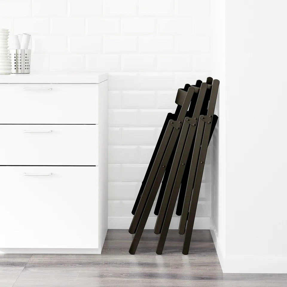 Foldable black chair stack against white wall; ideal for space-saving.