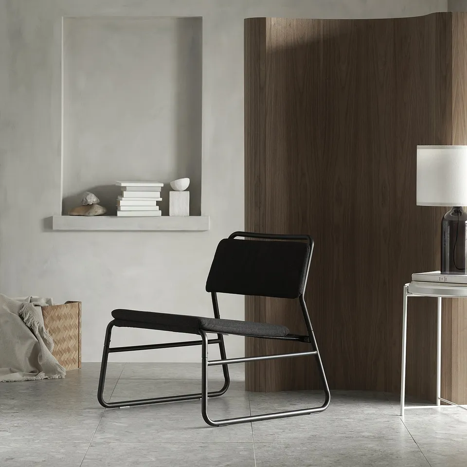 Minimalist room with black metal LINNEBÄCK chair, white lamp, wooden divider, grey floor, and grey-green wall.