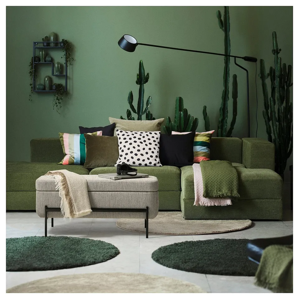 Cosy living room scene: green VALTORP sectional sofa with colourful pillows, small coffee table, and cactus decorations on olive green walls.