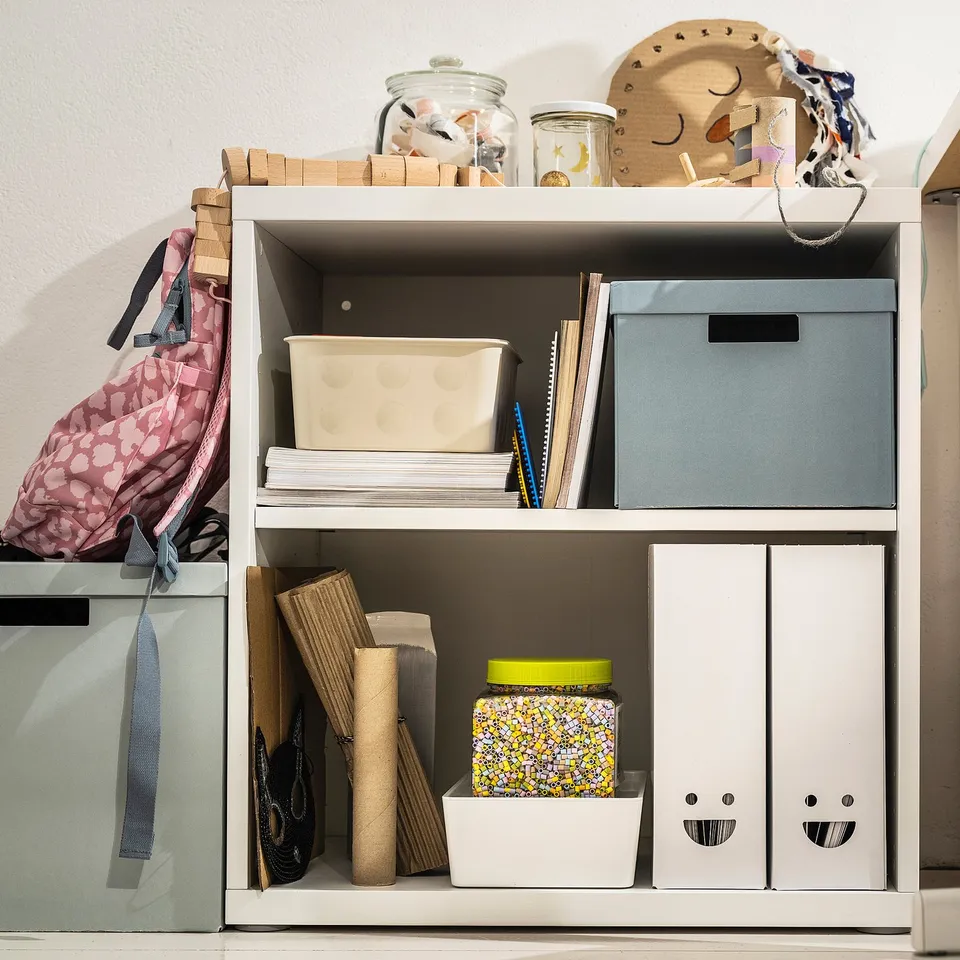 White bookshelf with TJABBA magazine files, boxes, jars, and fabric items.