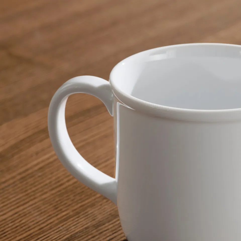 Clean white mug on wooden table, smooth handle, bright finish.