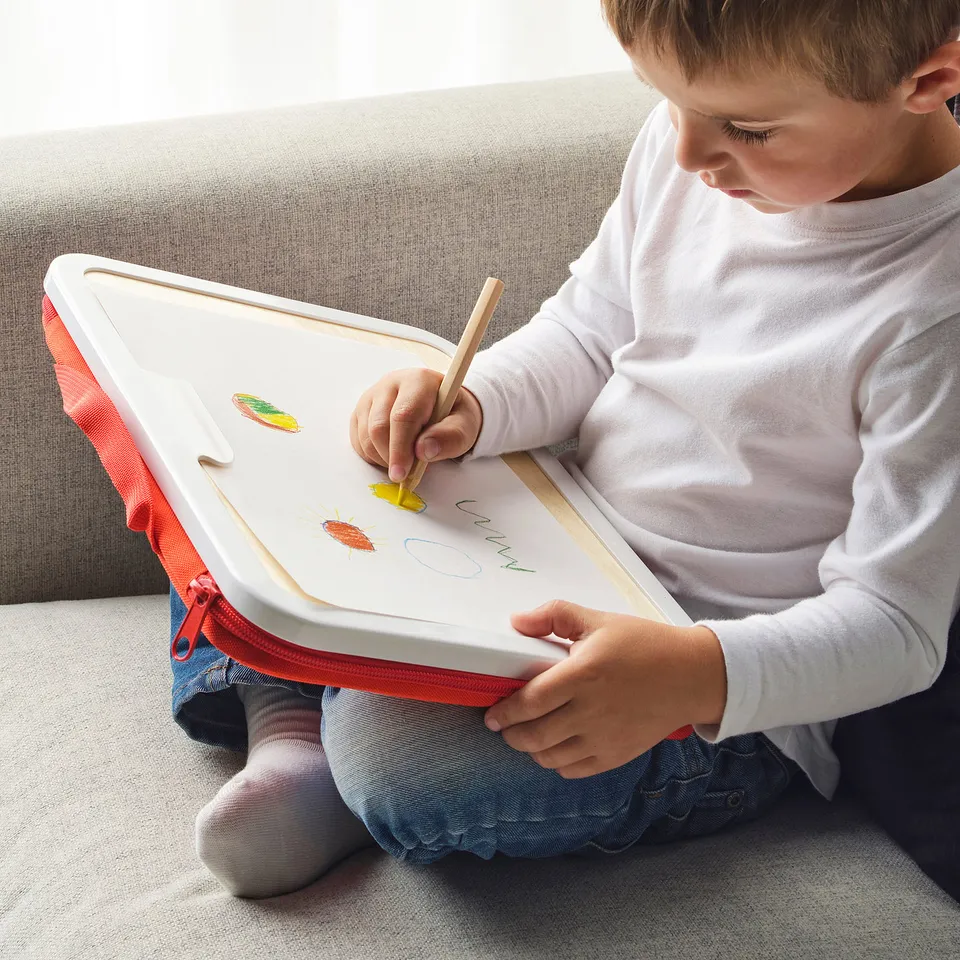 Child drawing on portable art case with wooden pencil.