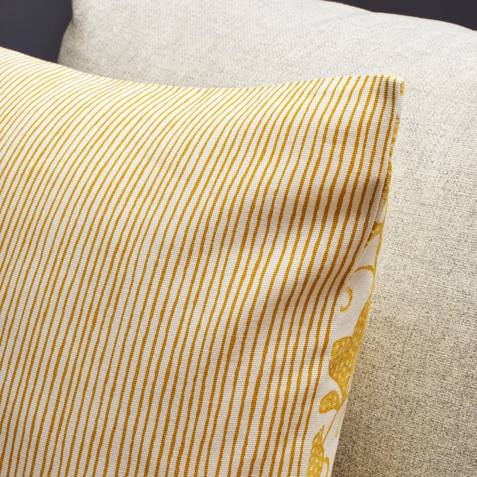 A close-up of a cushion cover with diagonal yellow stripes on one side and floral pattern on the other. Quality fabric and fine stitching visible.