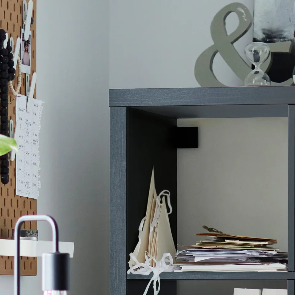 Grey KALLAX shelving unit with stacked papers, decorative items, and bulletin board with notes.