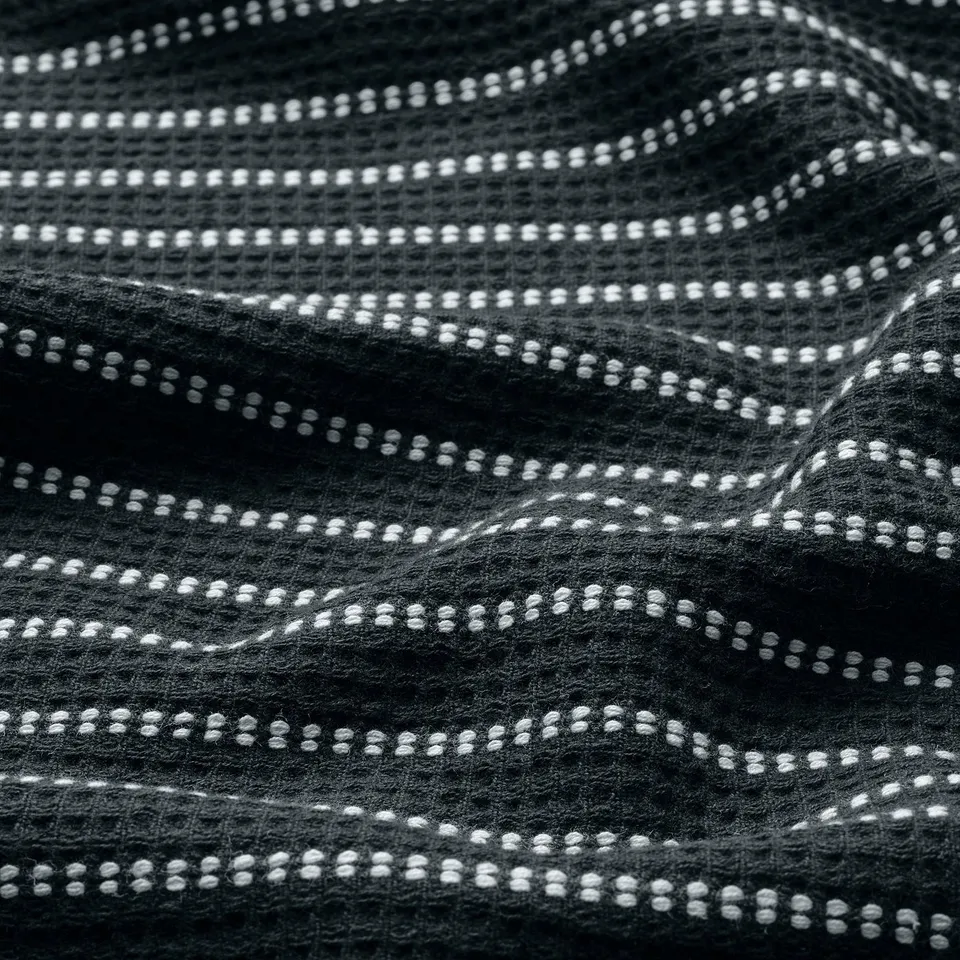 Textured black towel with white waffle pattern, soft terry side visible, crafted from 100% cotton.