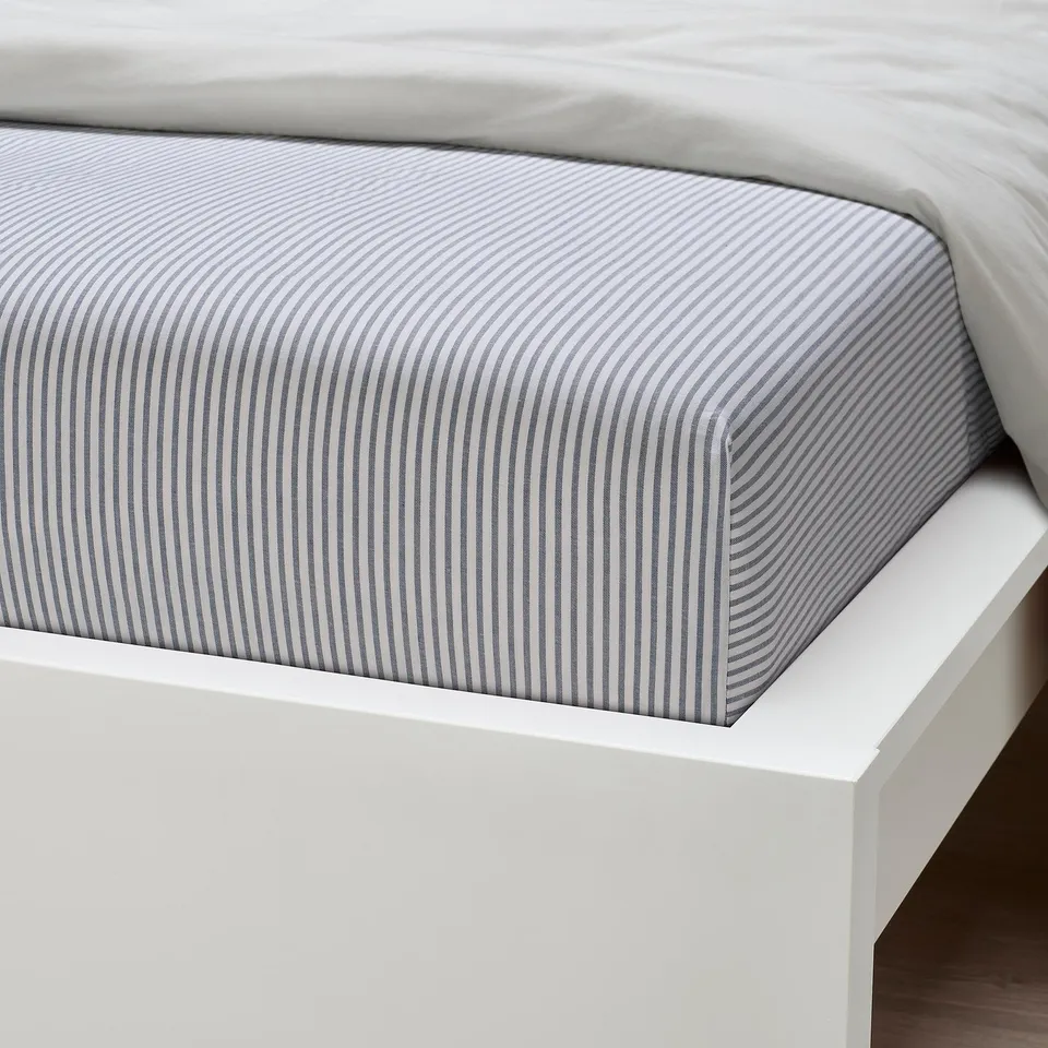 Crisp, white bed with blue-striped fitted sheet, neatly placed on a minimalist white bed frame.