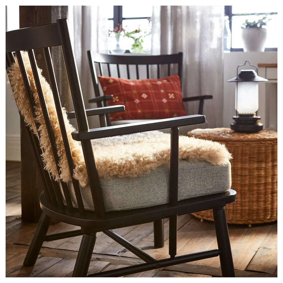 Cosy black rocking chair with cream sheepskin rug, red pillow, and lantern on wicker table.