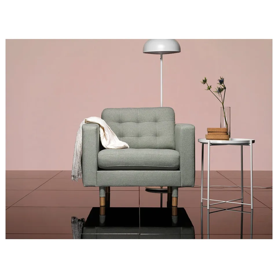 Modern living room a grey, upholstered armchair with wooden legs, positioned near a small table with a flower vase and lamp.