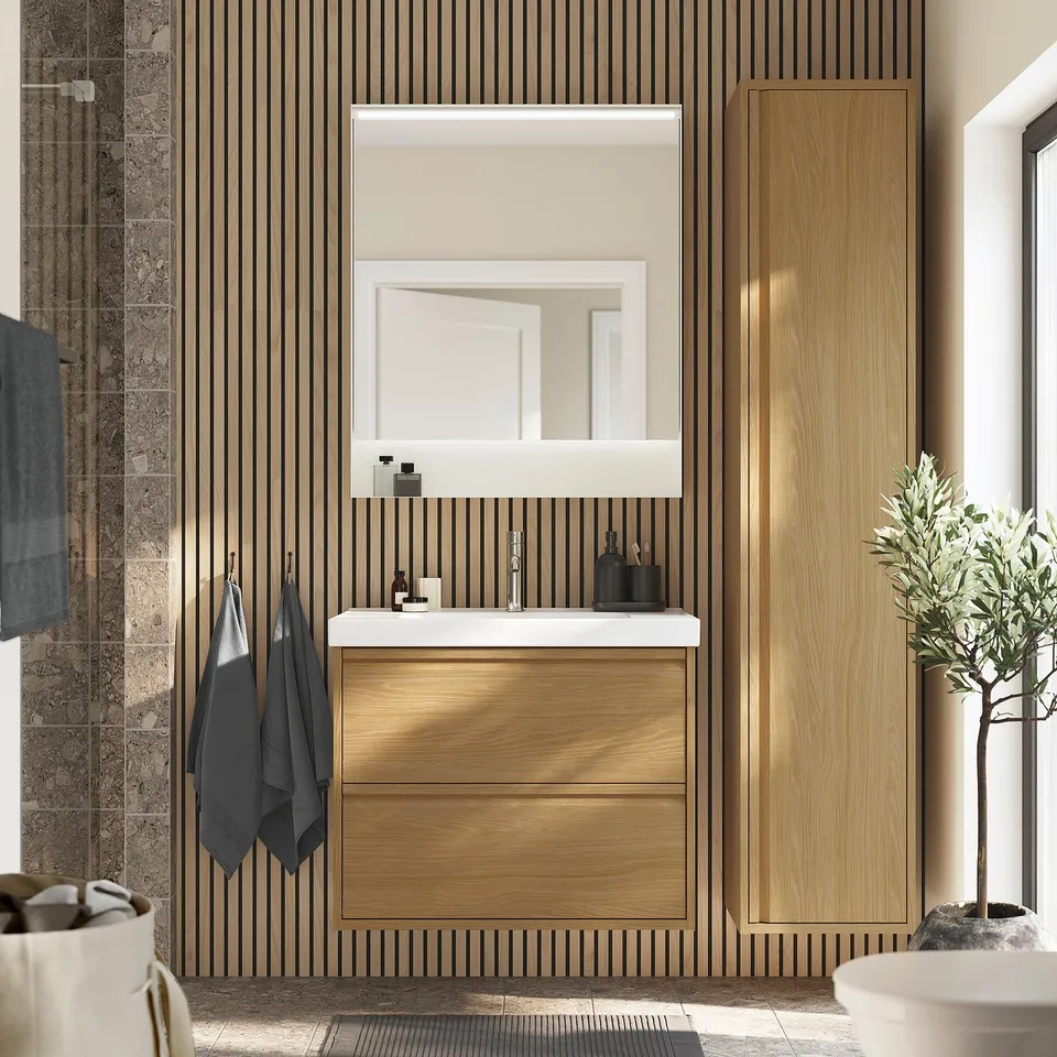 Modern bathroom with oak cabinet, white sink, large mirror. Floor plant, grey towels. Spacious, clean.