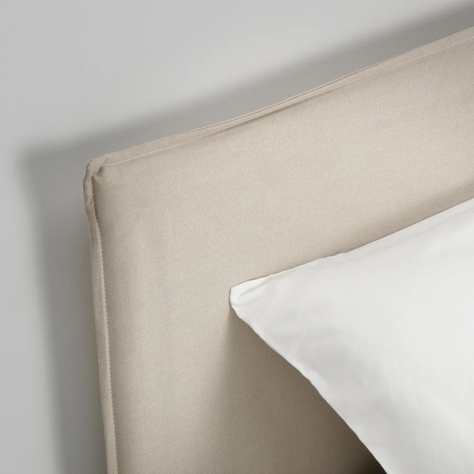 A close-up of a beige upholstered headboard with clean stitching and a white pillow, showcasing high-quality fabric and craftsmanship.