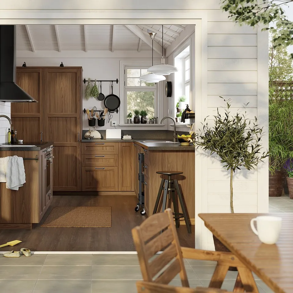 Modern kitchen with ENKÖPING brown walnut cabinets. Glass-fronted doors, wooden floors, white walls, and potted plants.