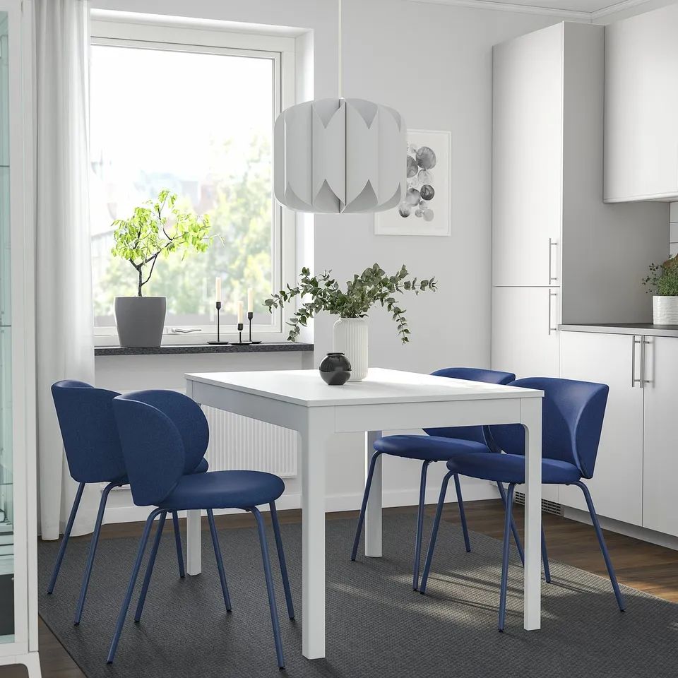 Modern dining room with white KRYLBO table, blue chairs, pendant lamp, and large window illuminating decor.