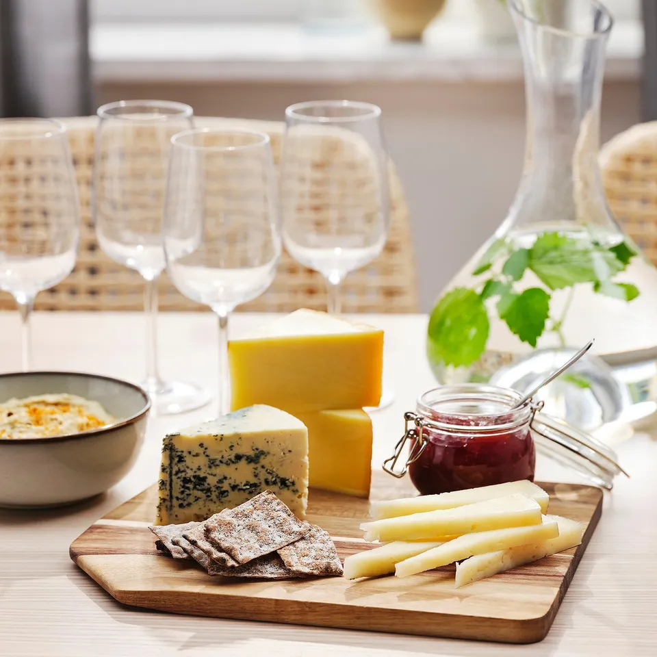 Wooden chopping board with cheese and crackers, surrounded by empty wine glasses, ready for a tasting event.