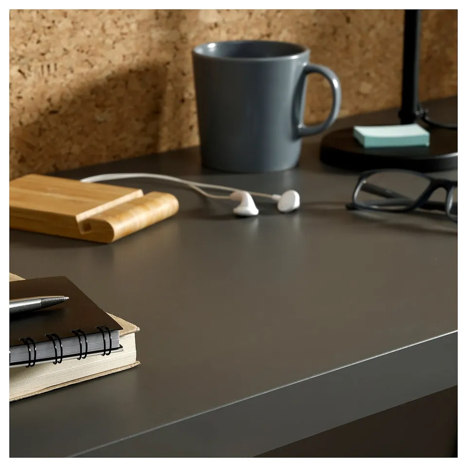Black desk with grey mug, glasses, and notepad. Modern, minimalist office setup.