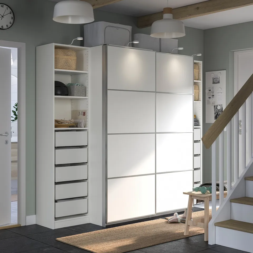 Modern room with white PAX wardrobe, shelves, and stairs. Lighting, storage, and wooden accents.