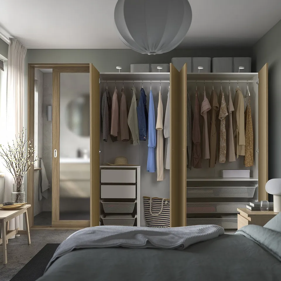Bedroom with open wardrobe displaying clothes, shelves, and organiser drawers. Soft lighting inside.