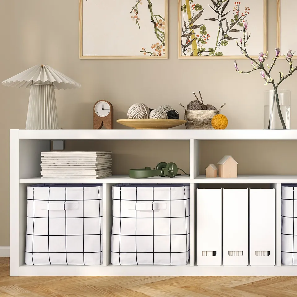 White KALLAX shelf with books, yarn, clock, and decor. Storage boxes for hiding items.