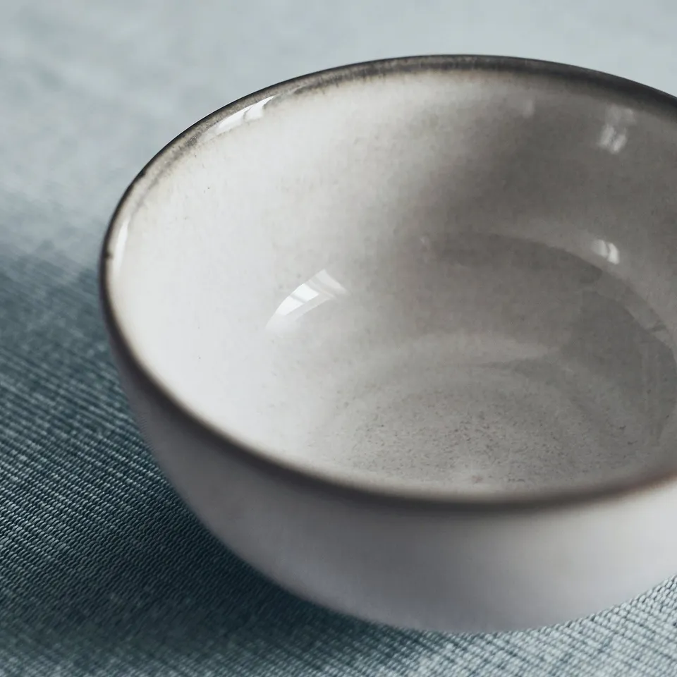 Empty grey-glazed bowl on a blue surface. Well-crafted, smooth edges, reactive glaze finish.