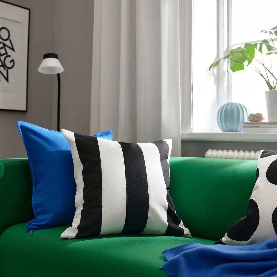 Bright green sofa with black-white striped, blue, and polka dot pillows. Large window with plant and decor.