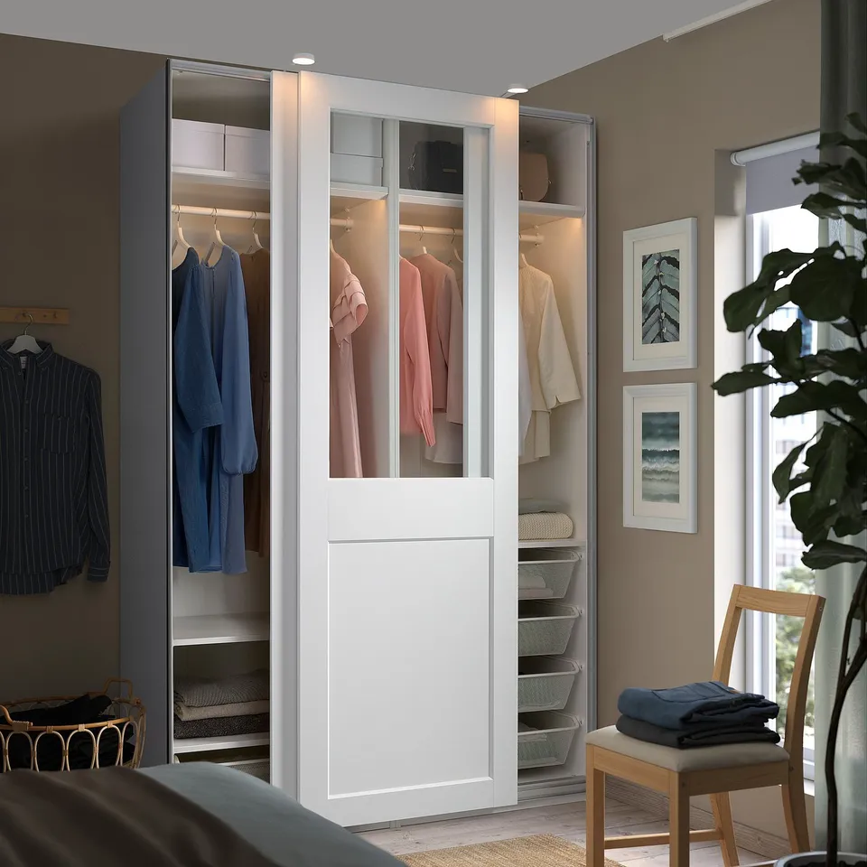 Modern bedroom with large PAX wardrobe, sliding glass doors exposing clothes, sleek white design.