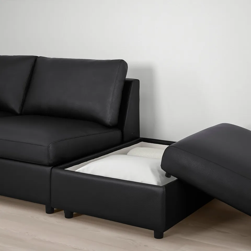 Black leather sofa with opened storage compartment showing white cushion inside.