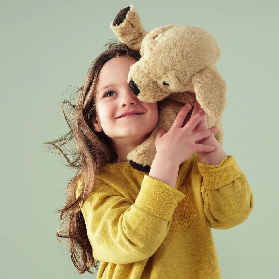 Girl in yellow sweater holding soft dog toy.
