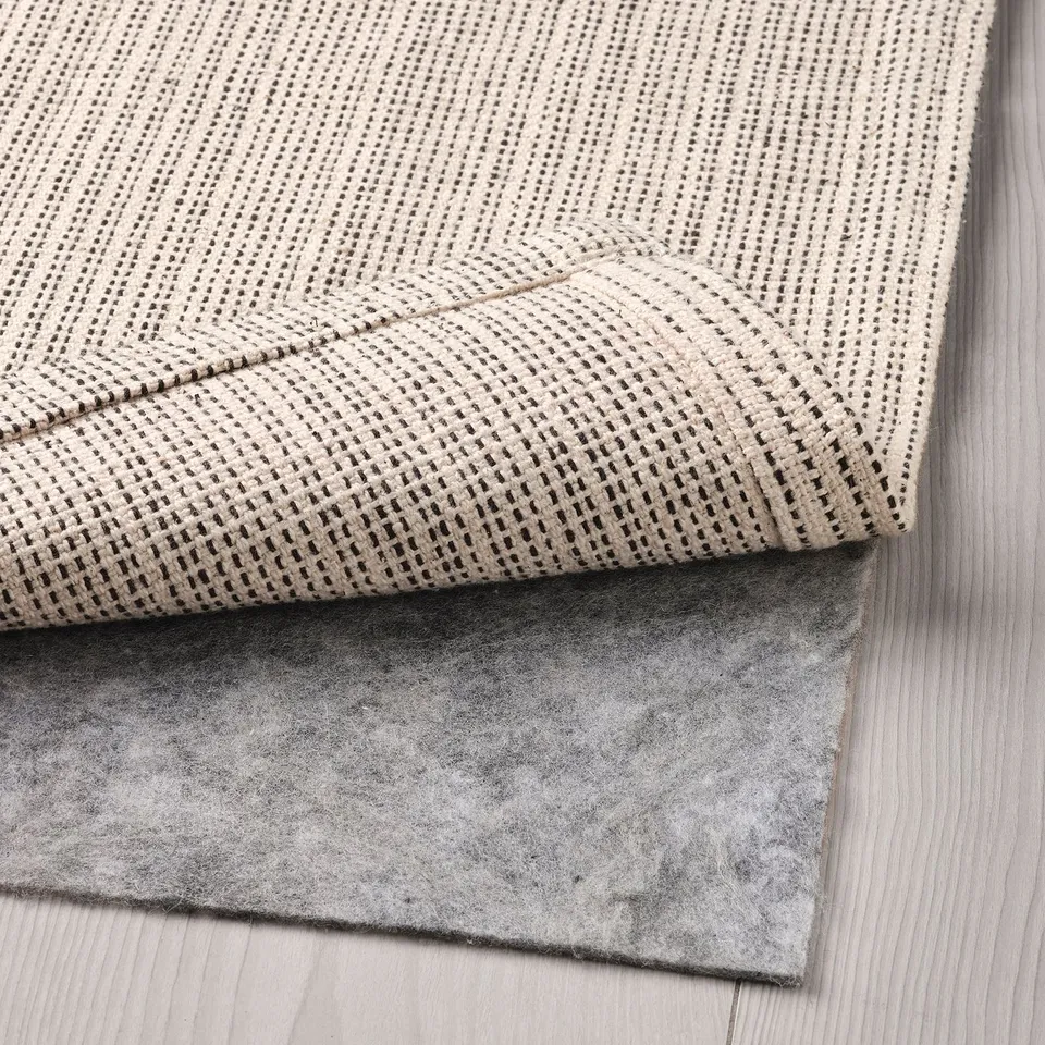 Folded beige cotton rug laid on wooden floor, showing its textured surface and backing mat.