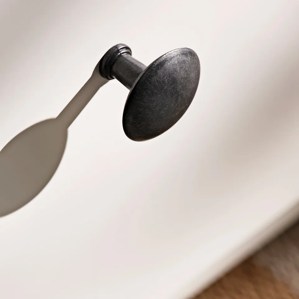 Black metal hook on white wall, holding a silver spoon.