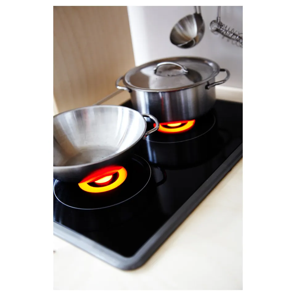 Silver pot and bowl on black toy stove with orange-red lights.