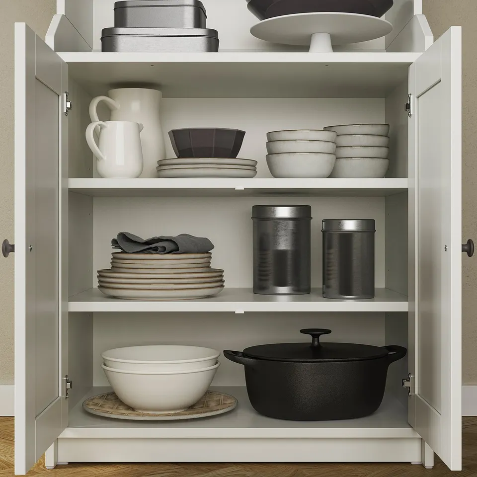 Open white cabinet with kitchenware. Includes mugs, bowls, pans, and stainless containers. Organised on three shelves.