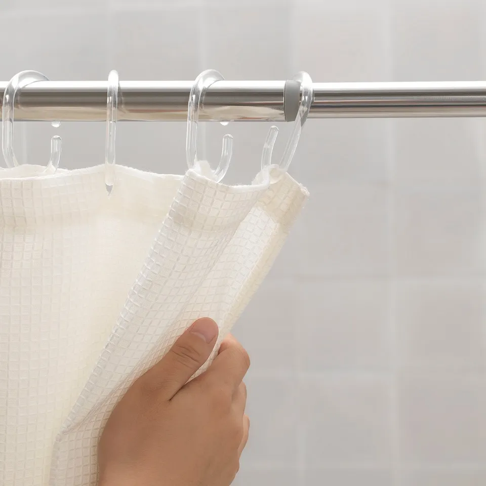 Hand holding white towel on stainless steel shower rod with clear hooks.